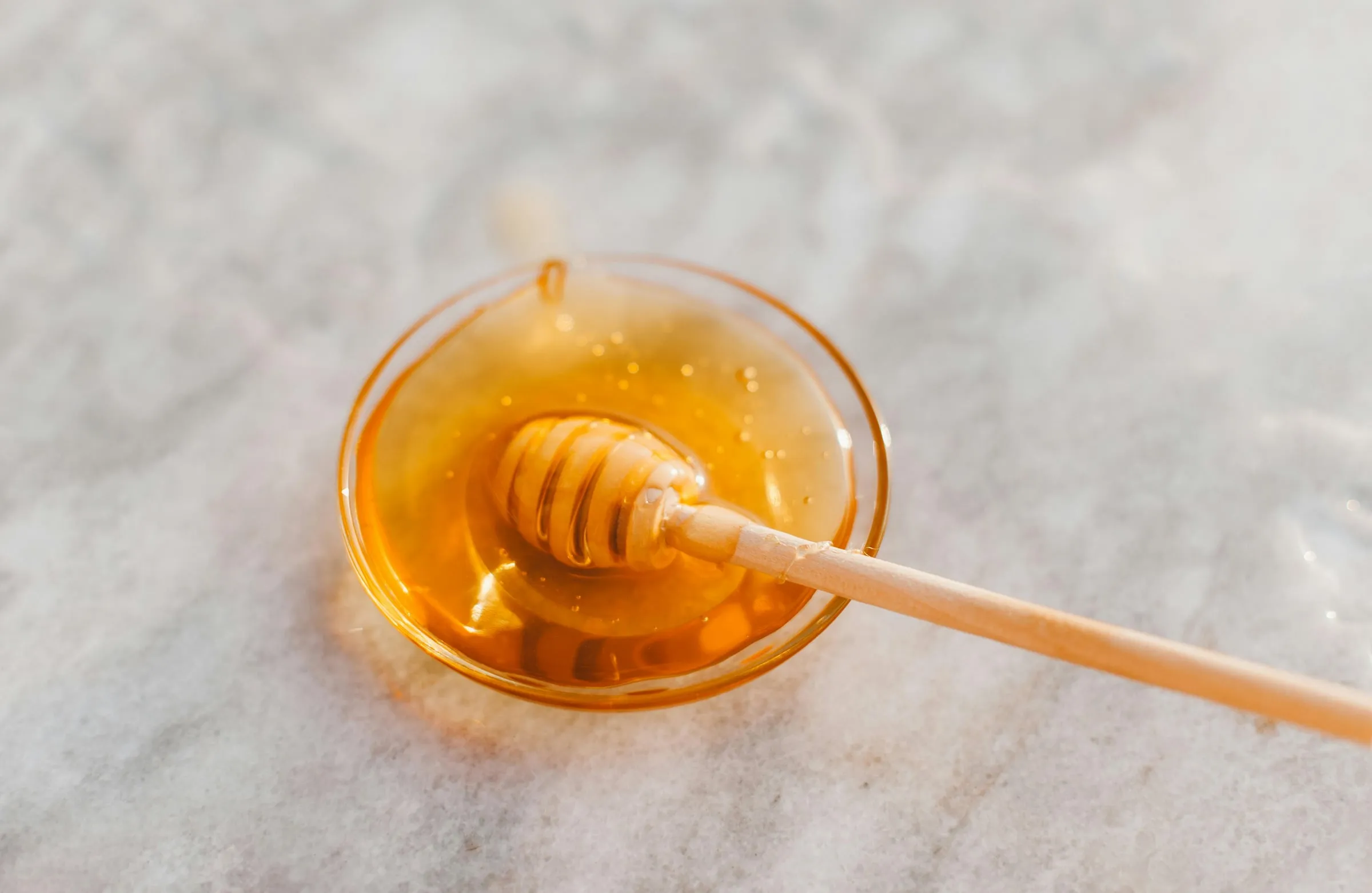 A bowl of honey with a wooden honey dipper